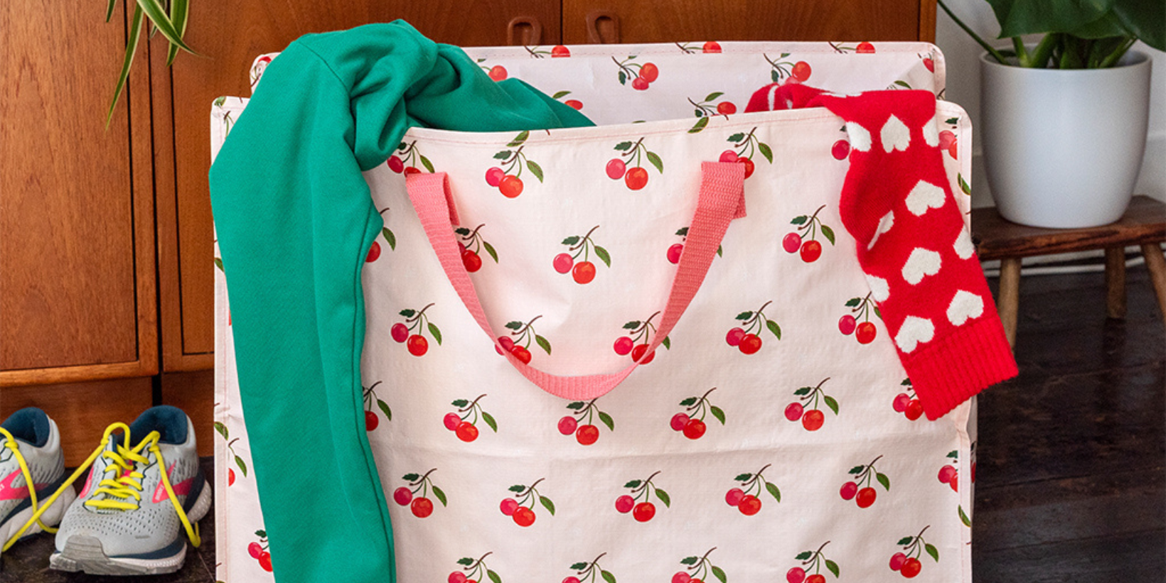A large storage bag with a cherry print is filled with clothes