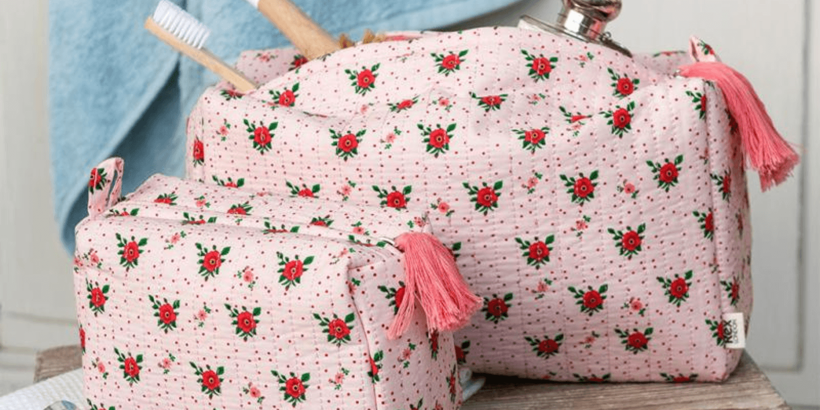 Two wash bags with a pink floral print sit on a wooden surface