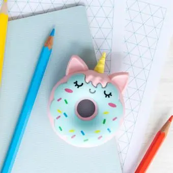 Doughnut-shaped unicorn eraser placed on a notebook beside coloured pencils.