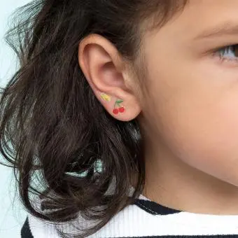 Stick-on earrings in cherry and lightning bolt shapes on a kid’s ear