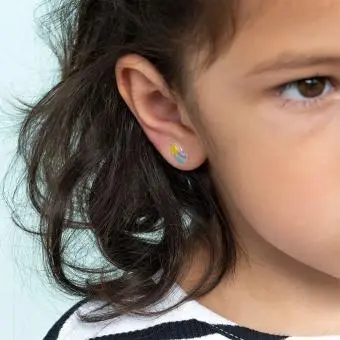 Stick-on earrings in rainbow shape on a kid’s ear