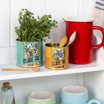 Two olive oil tins repurposed as herb and utensil holders on a kitchen shelf.