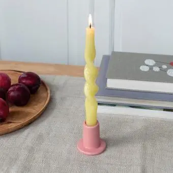 Pink ceramic candle holder with a cylindrical shape and wide flat base, holding a lit yellow candle