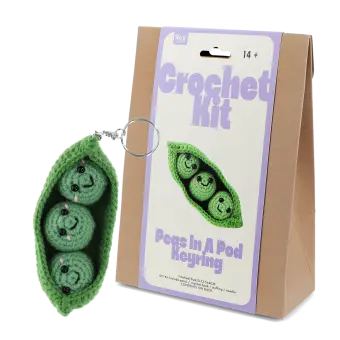 Crochet kit packaging placed beside finished green peas in a pod keychain 