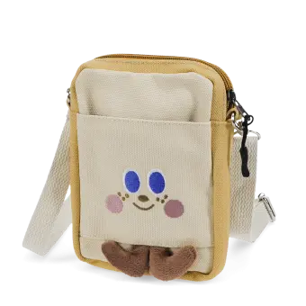 Beige and yellow crossbody bag with a front pocket featuring a smiling face design and two small brown plush feet at the bottom.