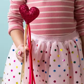 Kid holding a red heart wand with glittery top and ribbon streamers 