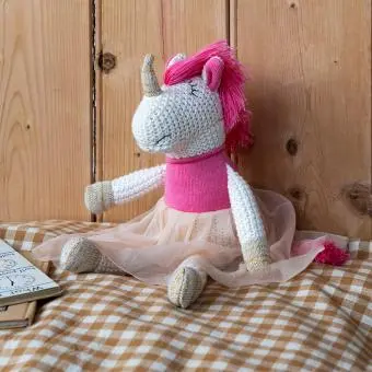 Knitted unicorn toy wearing a pink top and skirt