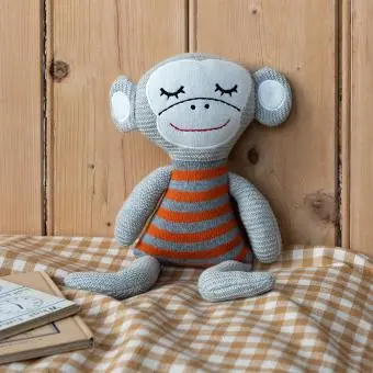 Knitted monkey toy with a grey body and wearing an orange and grey striped shirt.