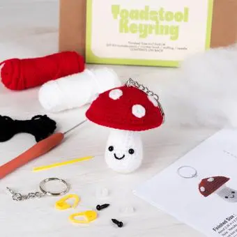 Crochet kit packaging displayed next to a finished red and white toadstool mushroom keychain