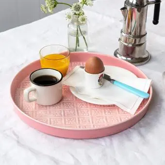 Round enamel trinket tray in pink displayed with cup of coffee, orange and an egg.