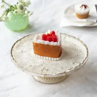 Heart-shaped cake candle with orange sides and red berry decorations displayed on a cake stand. 