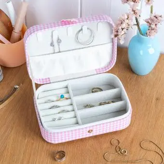 Pink gingham travel jewellery box with multiple compartments and slots displayed with some jewelleries.