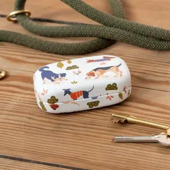 Mini travel case with playful dog illustrations on a wooden surface beside keys.