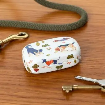 Mini travel case with playful dog illustrations on a wooden surface beside keys.