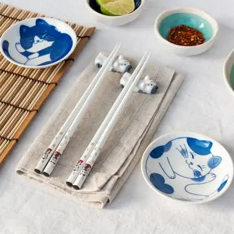 Two cat-themed dipping bowls, two pairs of chopsticks, and two cat-shaped rests.