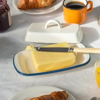 Rectangular white enamel butter dish with a blue rim and a handled lid displayed with butter.