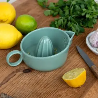 A green ceramic lemon juicer displayed with fresh lemons.