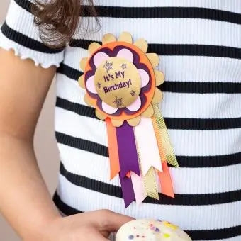 An “It’s My Birthday” badge attached to a child holding a wrapped gift.