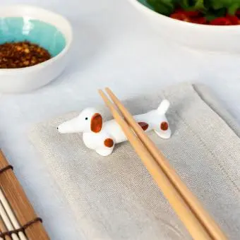 Chopsticks resting on a ceramic sausage dog–shaped chopstick rest.