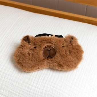 Light brown plush capybara‑shaped travel eye mask with stitched facial details