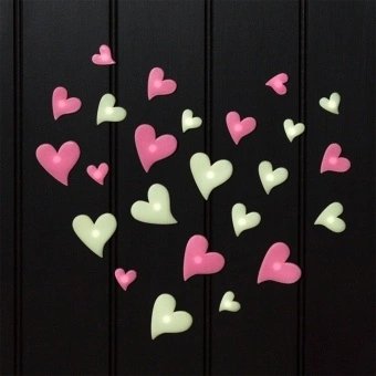 Pink and green glow‑in‑the‑dark heart shapes in assorted sizes on a black background.