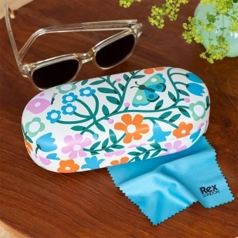 Esme floral-patterned sunglasses case with cleaning cloth on a wooden table.