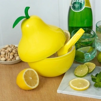 Pear-shaped ice bucket with lid and tongs, surrounded by citrus and drinks on a table.