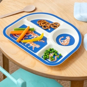 Tiger-themed toddler divider plate shown with vegetables, pretzels and peas on a wooden table.