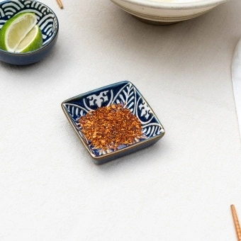 Square ceramic dipping bowl with a blue leaf pattern shown with chilli flakes.