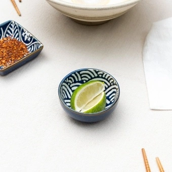 Round ceramic dipping bowl with blue wave pattern shown with lime wedges.