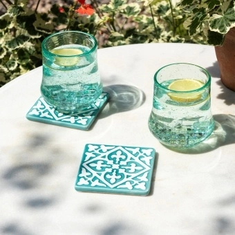 Turquoise ceramic tile coasters with white pattern beside two glasses of lemon water.