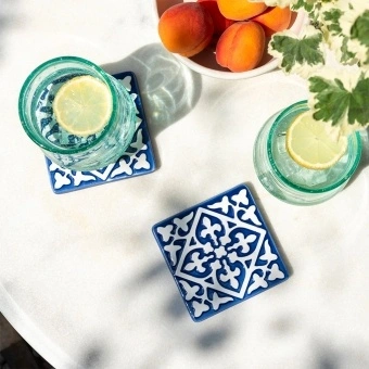 Blue ceramic tile coasters with white pattern shown beside two glasses of lemon water.