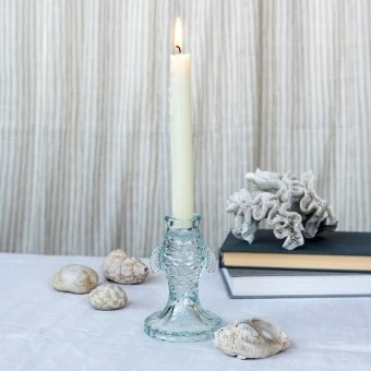 Pale blue fish-shaped glass candlestick holding a lit white candle on a tabletop