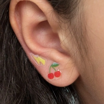 Stick-on earrings in cherry and lightning bolt shapes on a kid’s ear