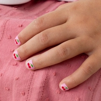 Red cherry printed nail stickers with pink background on a kid’s fingernails