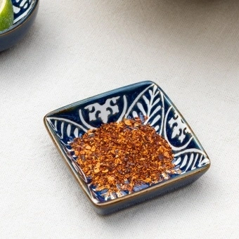 Square ceramic dipping bowl with a blue leaf pattern shown with chilli flakes.