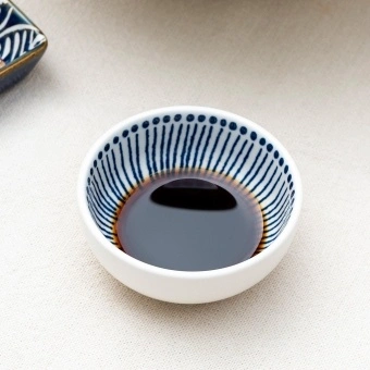 Round ceramic dipping bowl with blue line pattern shown with soy sauce.