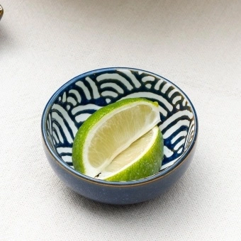 Round ceramic dipping bowl with blue wave pattern shown with lime wedges.
