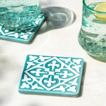 Turquoise ceramic tile coasters with white pattern beside two glasses of lemon water.