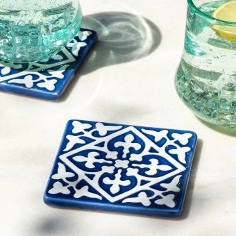 Blue ceramic tile coasters with white pattern shown beside two glasses of lemon water.