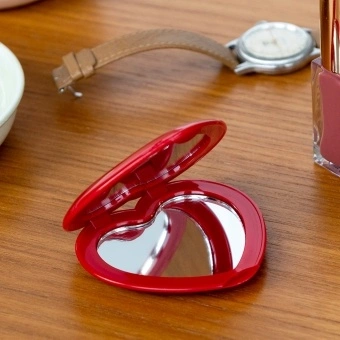 Red heart-shaped compact mirror on a wooden surface
