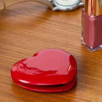 Red heart-shaped compact mirror on a wooden surface 