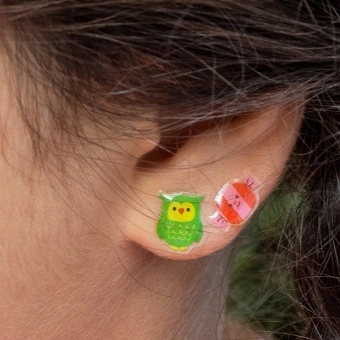 Colourful owl and bird stick-on earrings displayed on an ear.