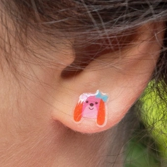 Pink dog-shaped stick-on earring with a blue bow displayed on an ear.