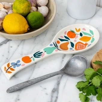 White ceramic spoon rest with a colourful fruit and leaf design.
