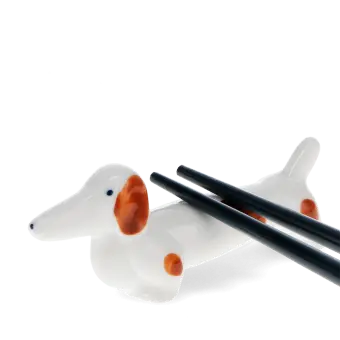 Chopsticks resting on a ceramic sausage dog–shaped chopstick rest.