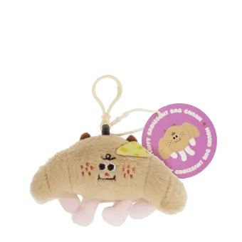 Fluffy croissant bag charm with smiley face, cheese patch and clip attachment with tag.